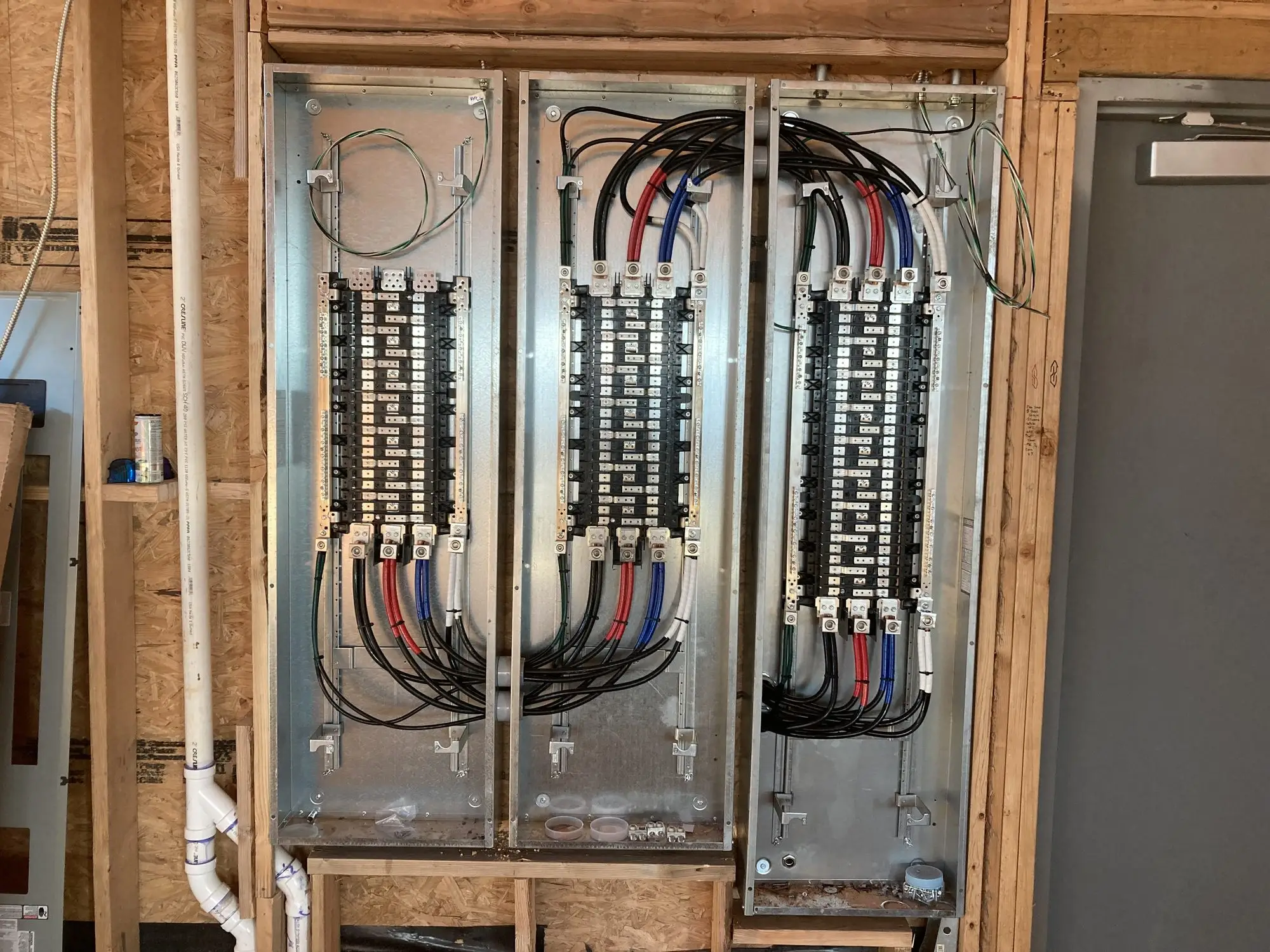 Three electrical panels mounted and wired in a stud wall during rough-in